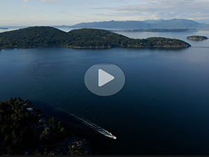 Screenshot from the Puget Sound Geographic Program video that shows a boat moving through Puget Sound with a semi-transparent play button superimposed on the screenshot to indicate this is a video